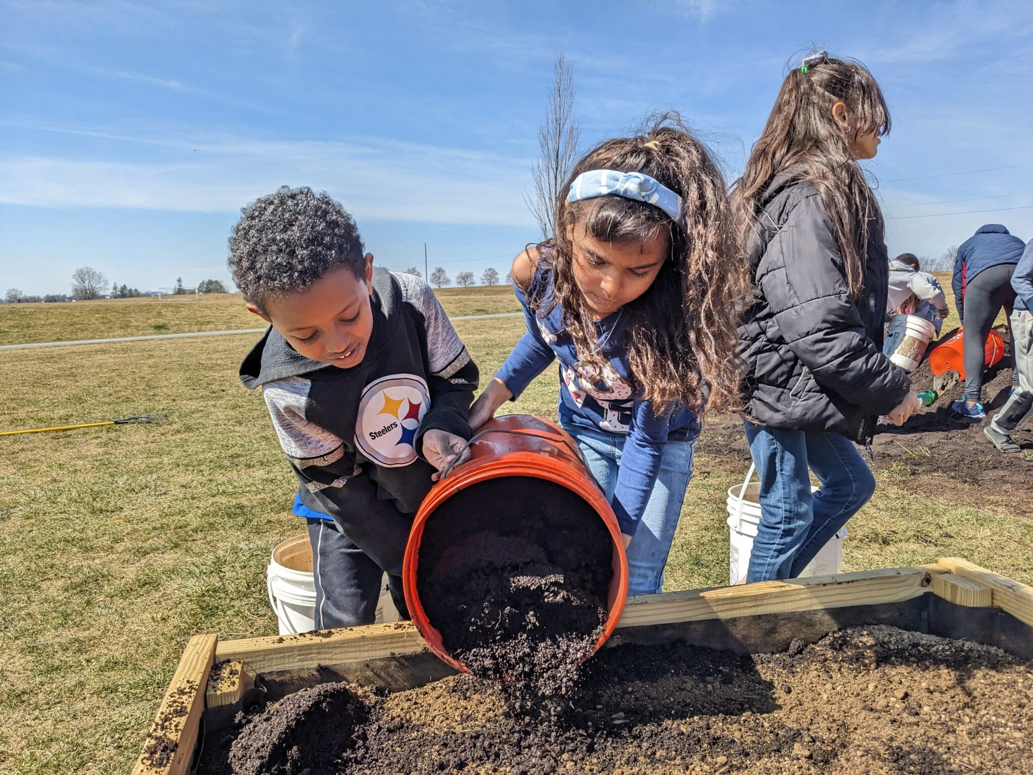 Photo of students filling garden beds with soil.