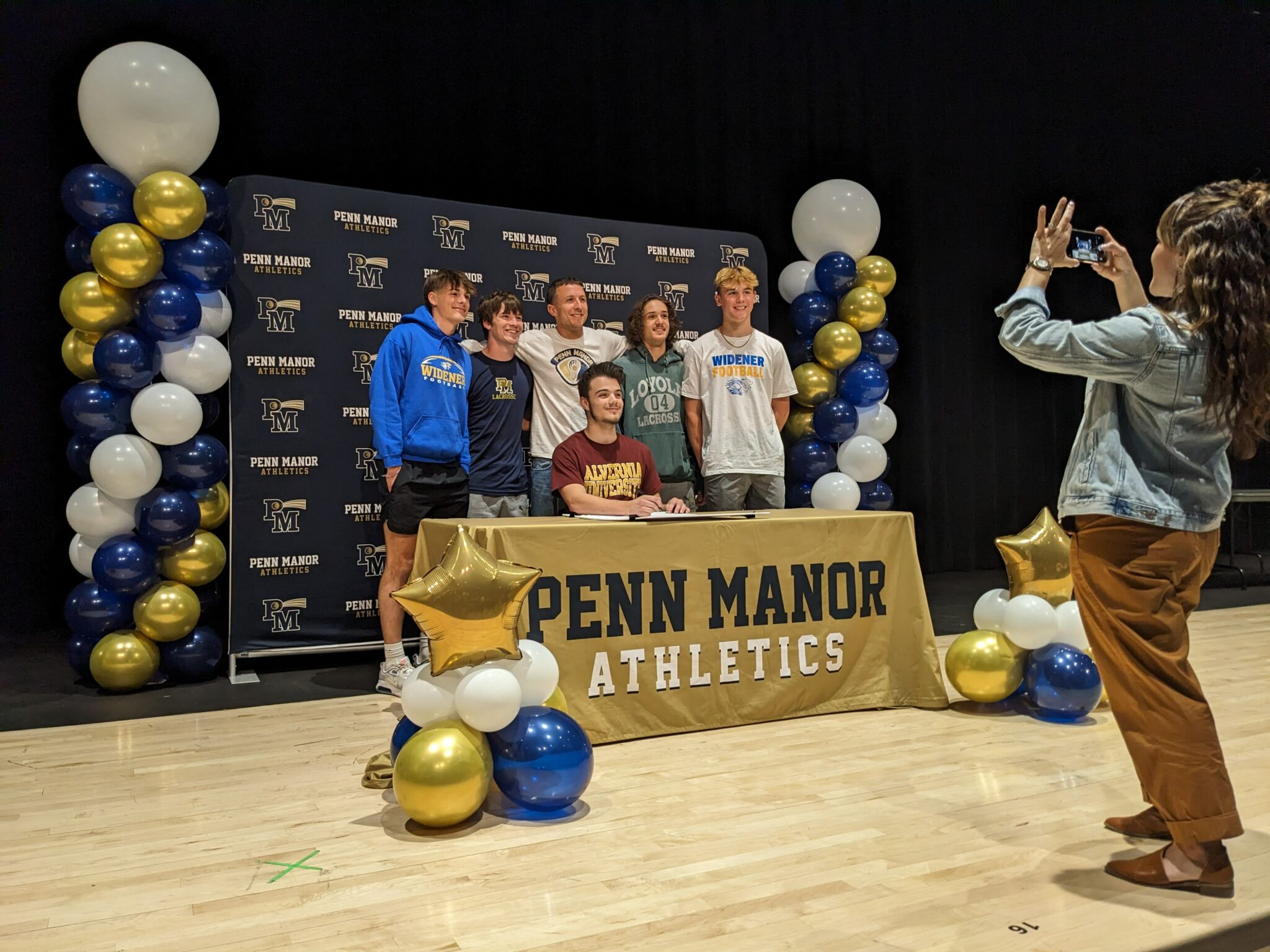 A parent takes a photo of six student athletes on the auditorium stage.