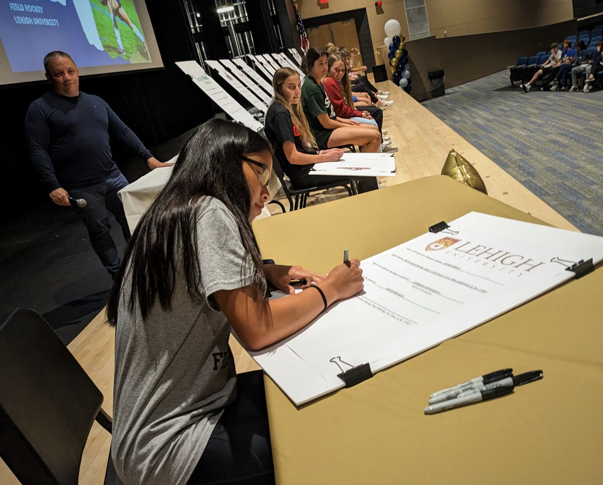 A student athlete signs a letter of commitment onstage.