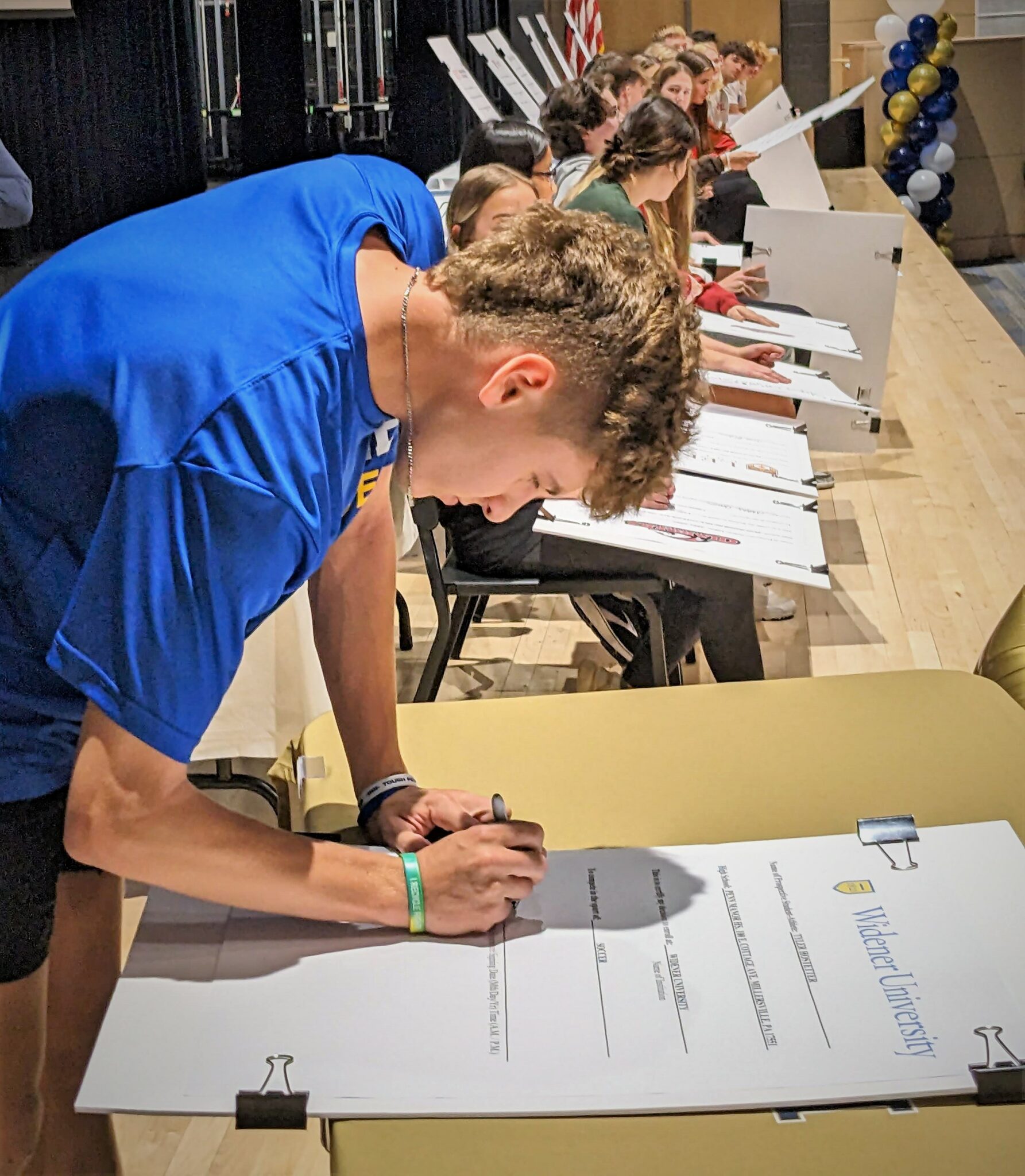 A student athlete signs a letter of commitment onstage.