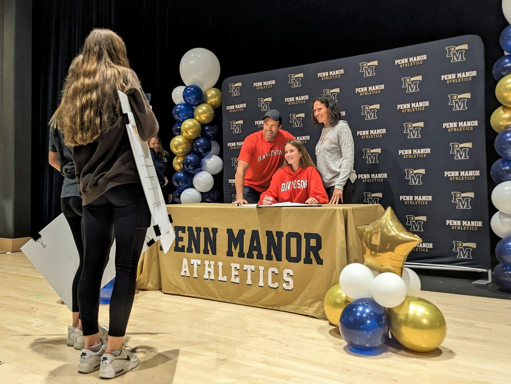 a student takes a photo of a student athlete and her parents.