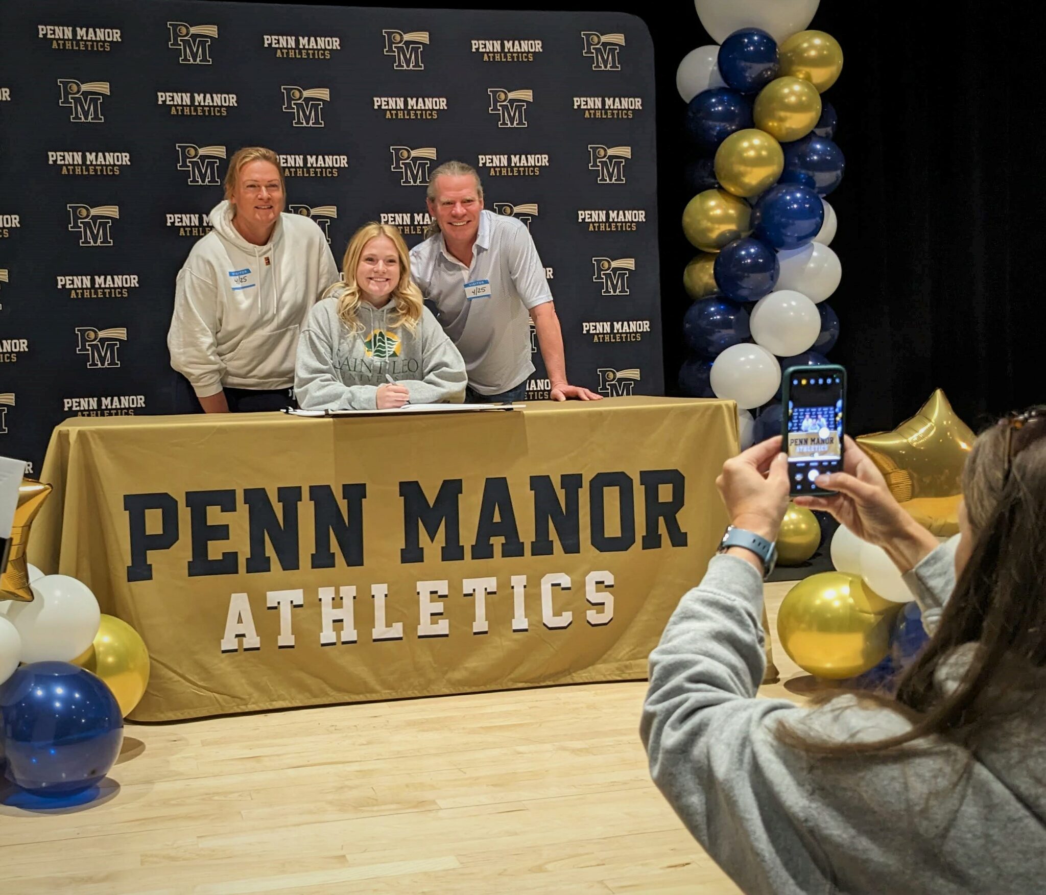 a student takes a photo of a student athlete and her parents.