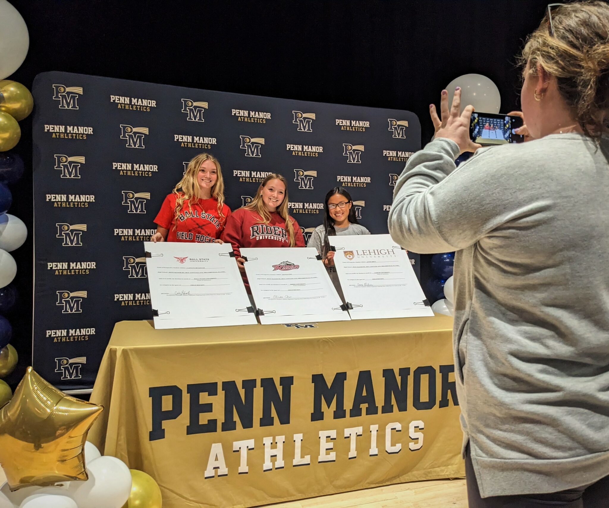 A coach take s a photo of three student athletes