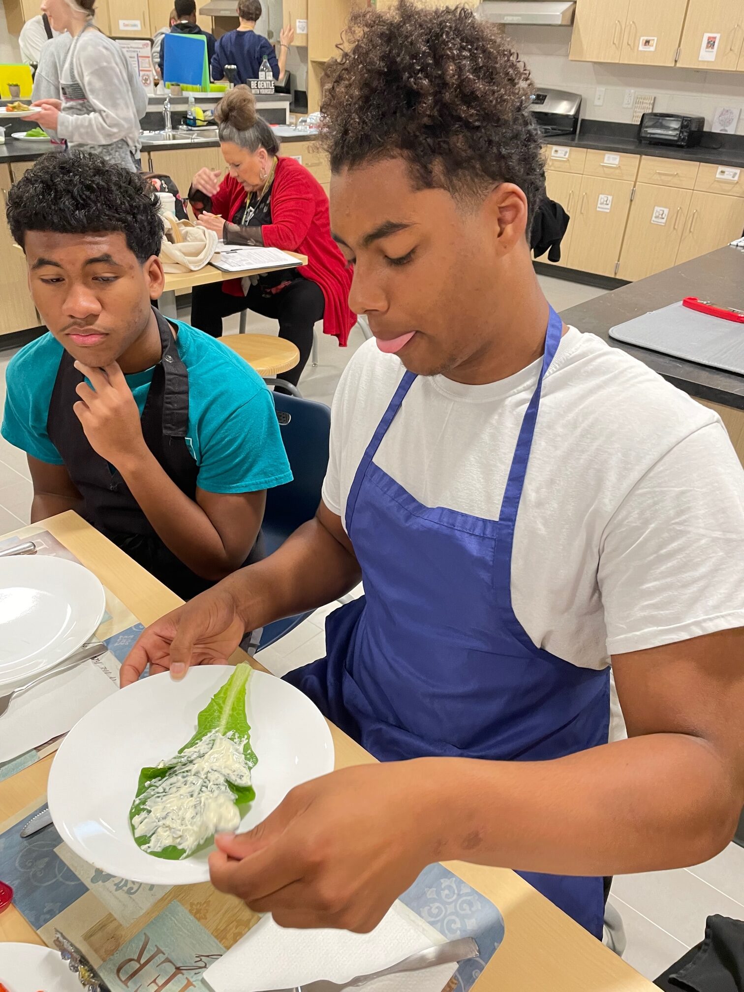 Photo of two students preparing to taste a piece of lettuce with aioli.